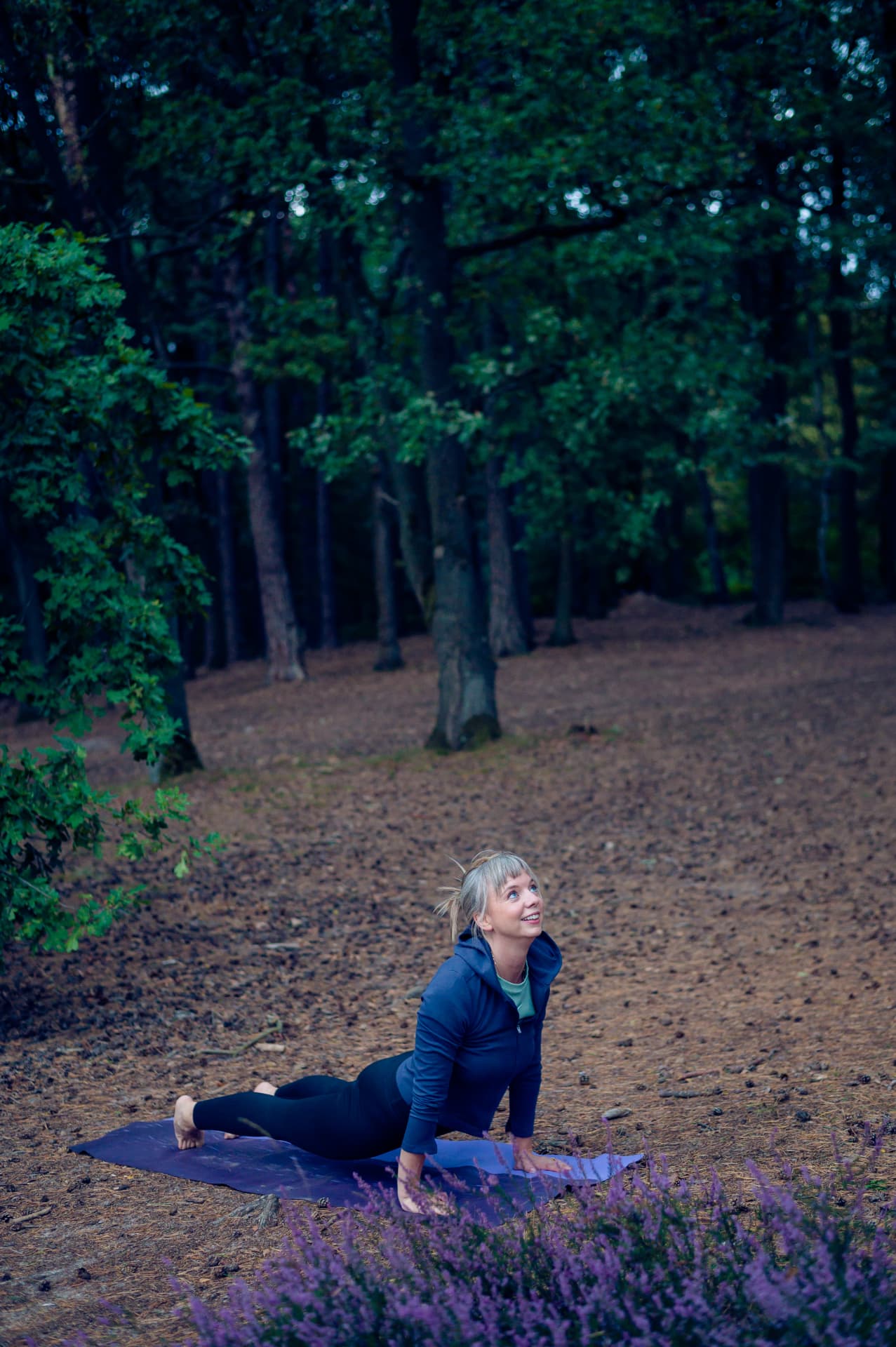 Ethel ligt met gebogen knieën en handen op haar buik op een blauwe mat in het bos